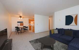 Fargo, ND Sugar Plum Apartments. A living room with a navy blue couch, a coffee table, and a dining area with a table and four chairs in the background.