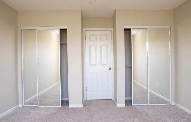 an empty bedroom with mirrored closets and a white door