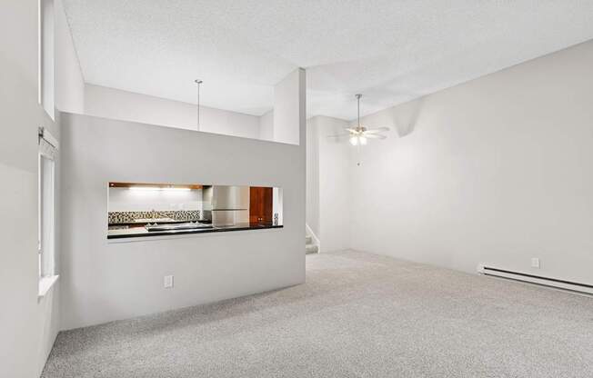 A spacious room with a carpeted floor and a window with a view of a kitchen.