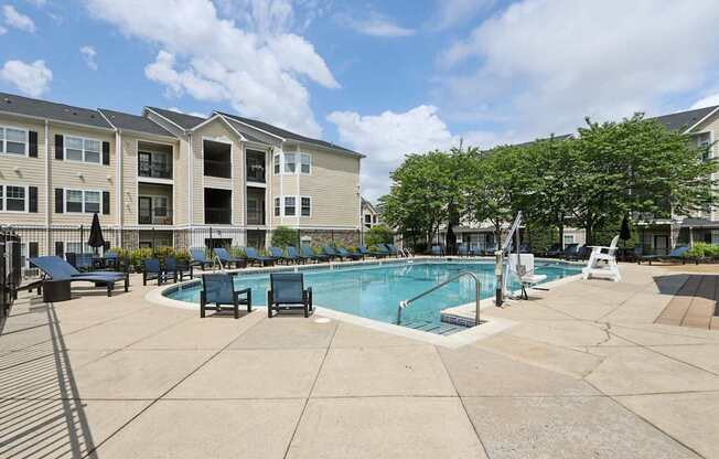 A large swimming pool surrounded by lounge chairs and trees in front of apartment buildings.