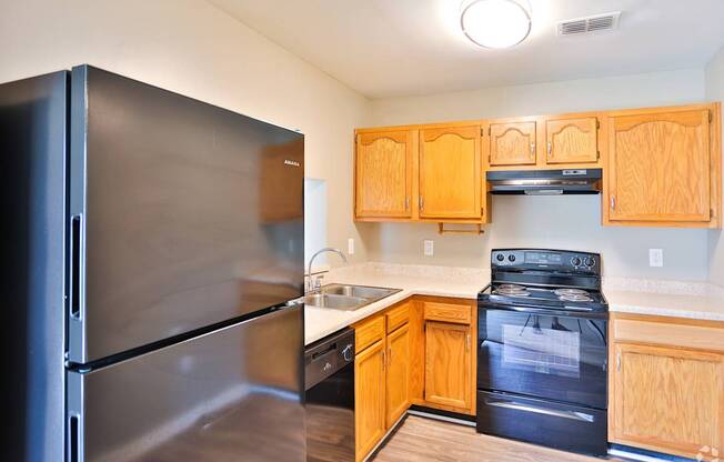 A kitchen with a black refrigerator and wooden cabinets.