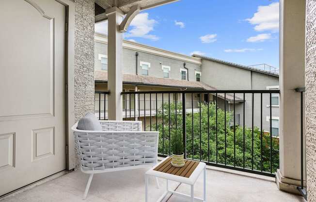 A white chair and table are on a balcony with a view of a building.