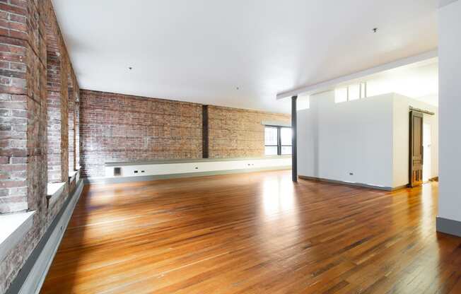 an empty living room with wood floors and a brick wall