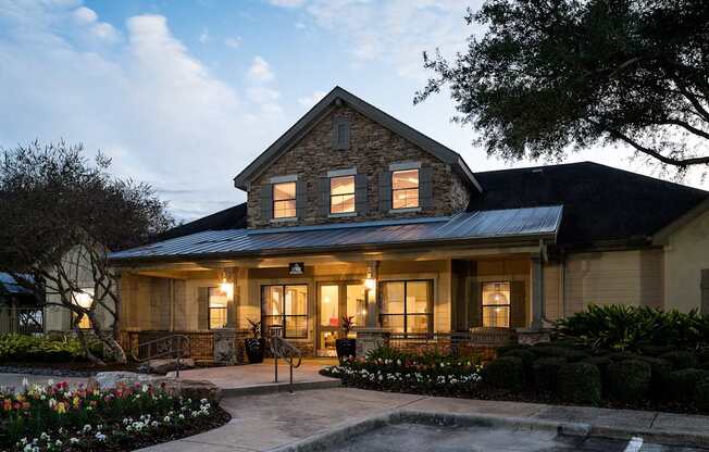 A house with a stone facade and a grey roof is surrounded by a garden with a fountain.