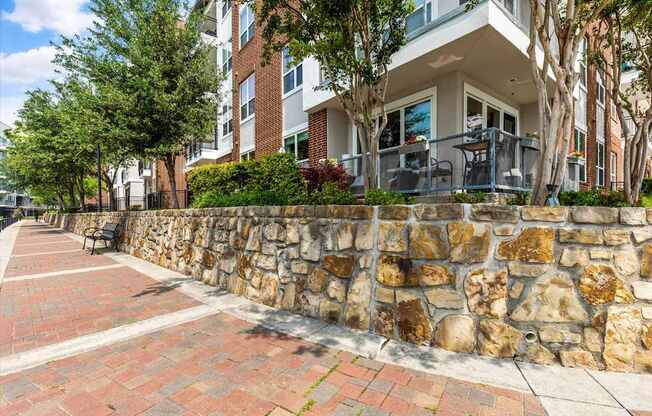 A stone wall separates a sidewalk from a grassy area in front of a building.