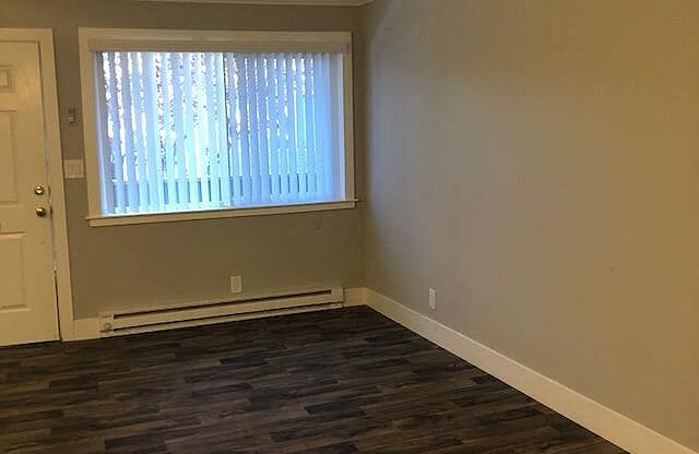 A room with a window covered by white blinds and wooden flooring.