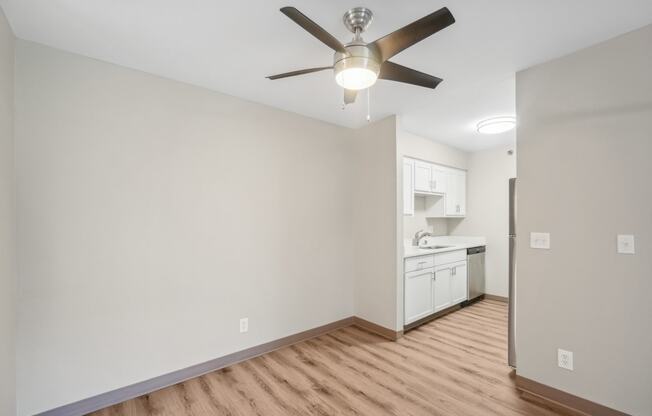 an empty living room with a ceiling fan and a kitchen