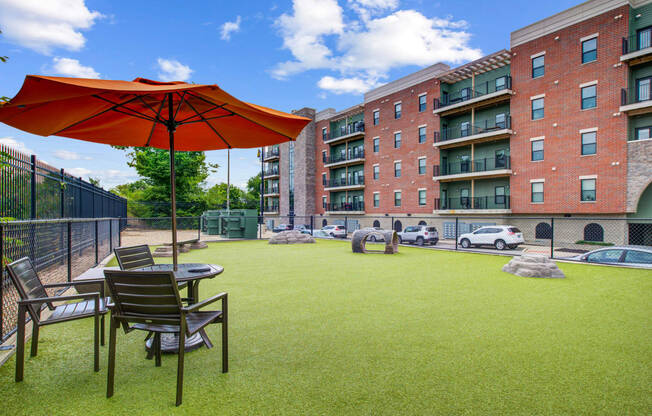 A fenced in dog park with a table, umbrella, and chairs at The Vue Luxury apartments in Indianapolis