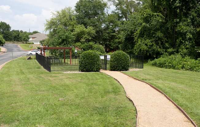 View of gated dog park with pergola and seating underneath and wooded area in background