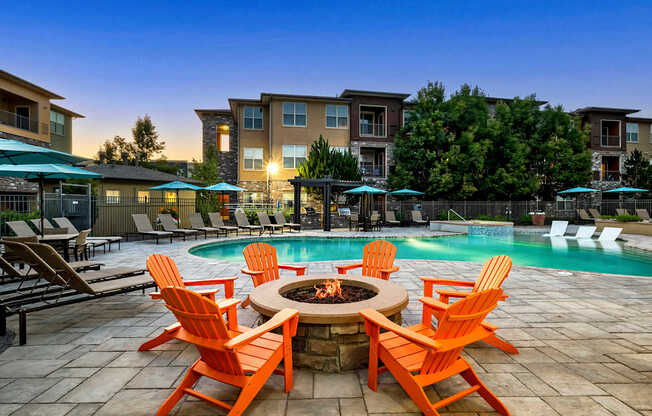 A poolside patio with orange chairs and a fire pit.