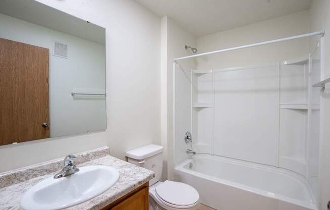 A white bathroom with a sink, toilet, and bathtub. Bismarck, ND Sierra Ridge Apartments