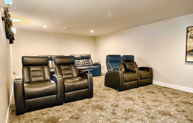 A private theater room here at Andorra featuring rows of plush black reclining seats with built-in cup holders, soft patterned carpeting, neutral walls, and recessed ceiling lighting, creating a comfortable and inviting space designed for movie nights, group screenings, and relaxed entertainment for residents.