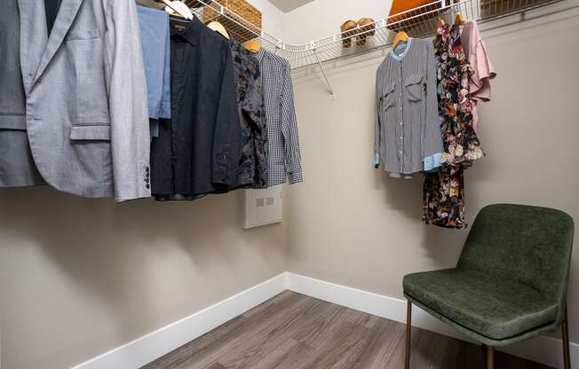 a walk in closet with a chair and clothes hanging on the wall