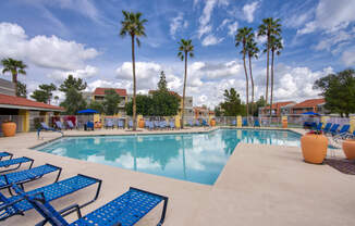 a large swimming pool with blue chaise lounge chairs and palm trees in the background