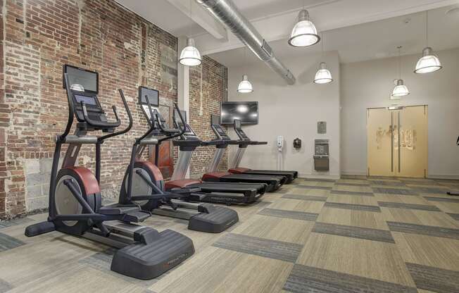 a row of treadmills in a gym with a brick wall