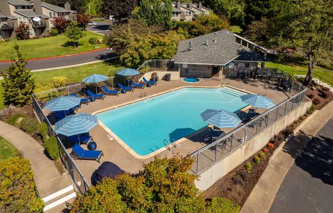 an aerial view of a swimming pool with blue chairs and umbrellas around it