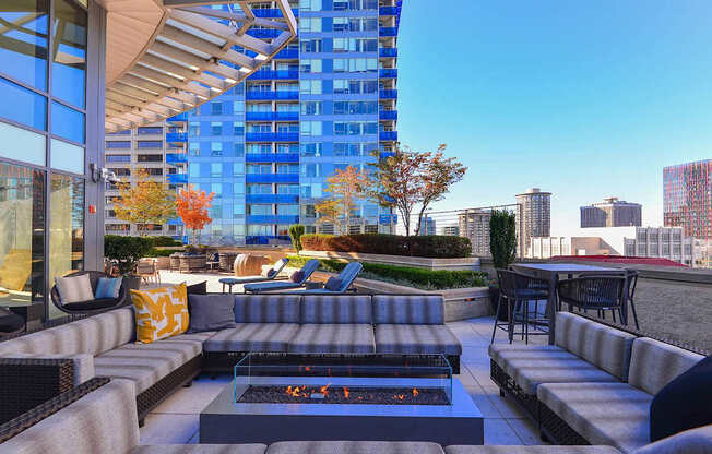 A patio with a fire pit and seating area with a view of a city skyline.
