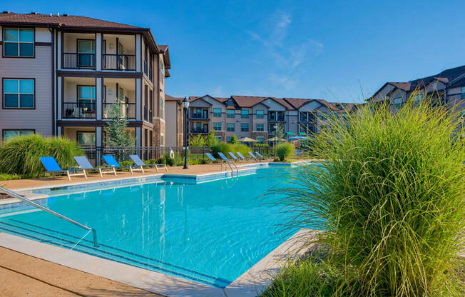 A large swimming pool with the apartments surrounding it and beach chairs