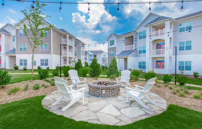 A fire pit surrounded by four chairs in a grassy area in front of apartment buildings.