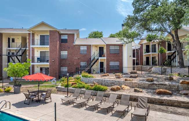 A pool area with chairs and a red umbrella in front of apartment buildings.