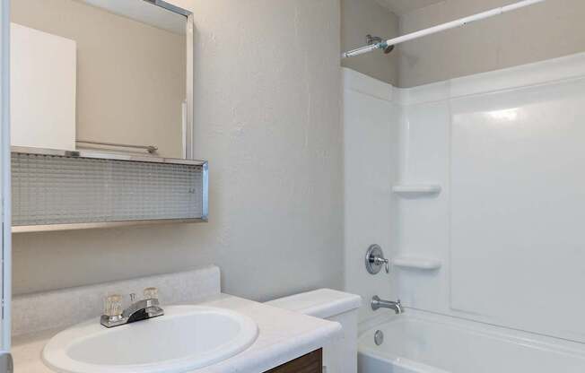 A white toilet with a brown cabinet and a white sink with a mirror above it.