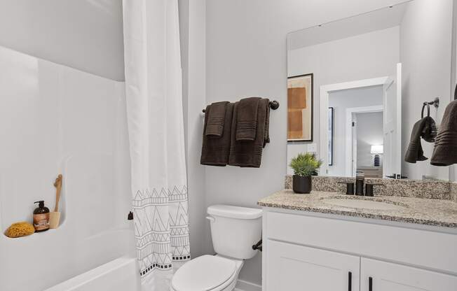 a bathroom with a granite topped vanity, toilet, and a tub/shower