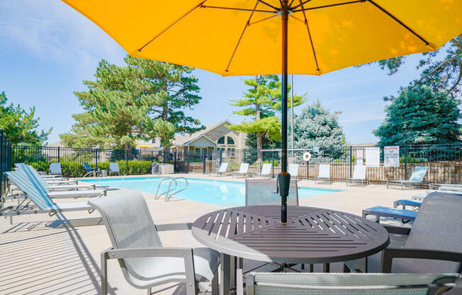 outdoor dining table and chairs shaded with a yellow umbrella next to the swimming pool