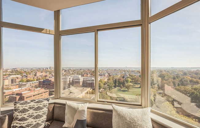 A couch with a pillow sits in front of a large window with a view of a city.