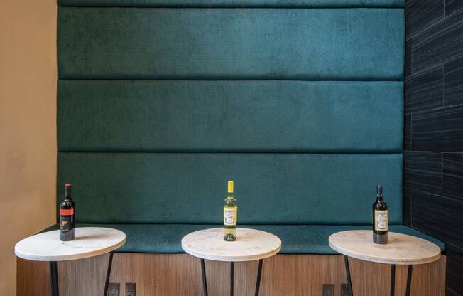 a trio of tables in front of a teal wall with two bottles of wine on top