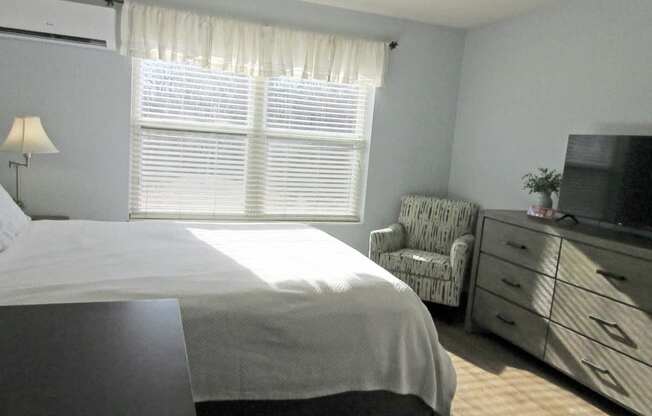 A bedroom with a bed, chair, and television.