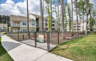 a fenced in dog park in front of an apartment building