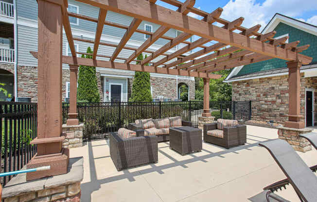 a covered patio with couches and chairs under a wooden pergola