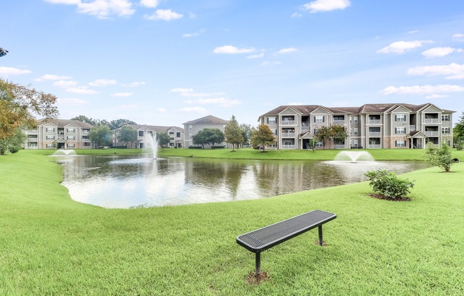 a bench sits in front of a pond with a fountain and apartment buildings in the background at Plantation Crossing, Louisiana, 70508