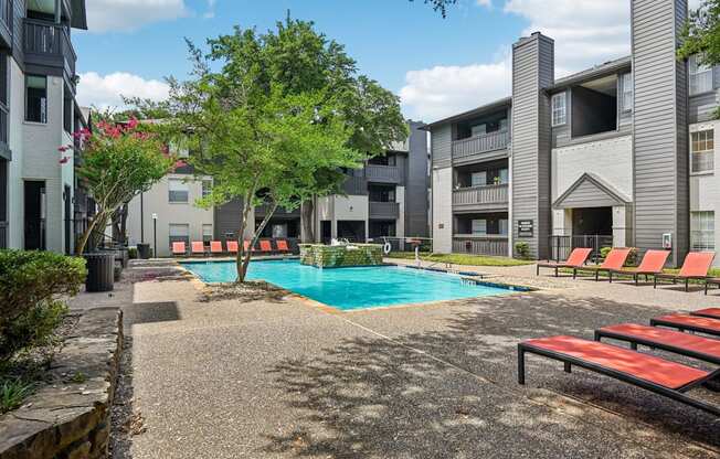 A pool surrounded by apartment buildings and trees.