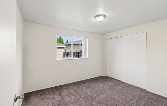 A room with a window showing a view of a building and trees outside.