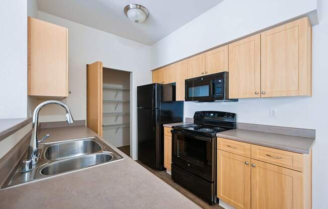Soho kitchen with black appliances, a pantry closet, and wooden cabinets at Abbey Rowe Apartments in Olympia, WA