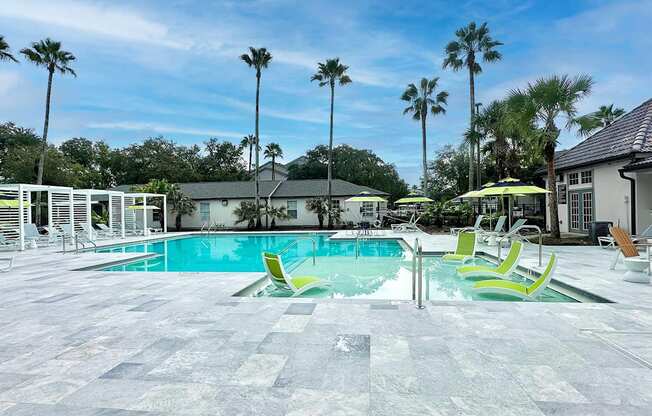A pool area with a tiled floor and palm trees in the background.
