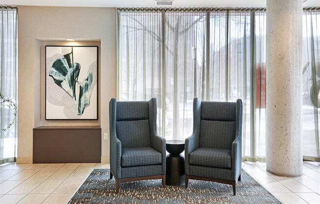 Two grey chairs are placed on a rug in front of a large window.