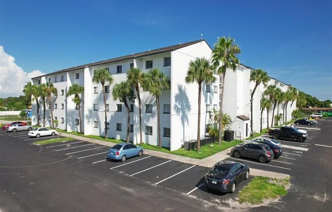 a large white building with palm trees in front of a parking lot