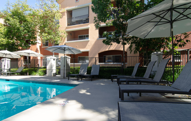 A pool surrounded by chairs and umbrellas with a building in the background.