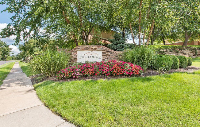 a sign for the home is in front of a sidewalk and flowers at Lodge of Overland Park Apartments, Kansas