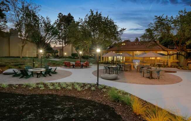 a patio with tables and umbrellas at night at Summerwood Apartments, Santa Clara, CA