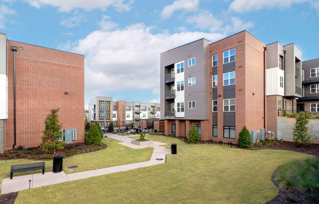 A modern apartment complex with a grassy courtyard and a bench.
