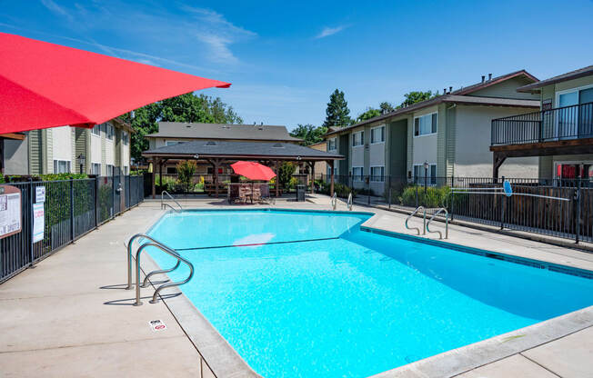 View of gated community pool with seating under umbrellas and covered area with picnic table and seating