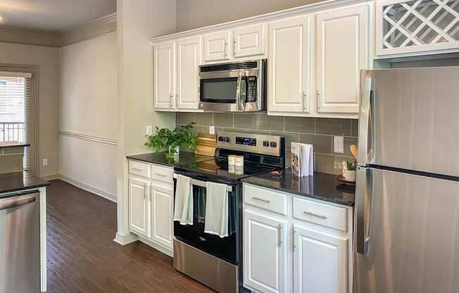 A kitchen with a black granite counter top and white cabinets in the 1486 square foot 3 bedroom, 3 bath apartment with attached 2-car garage at The Brownstones in Far North, Dallas, Texas