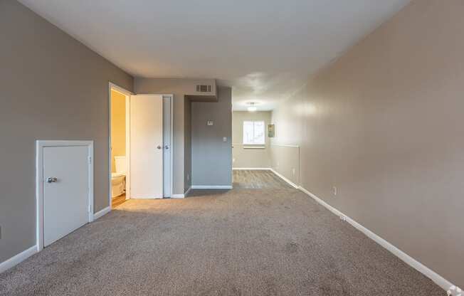 an empty living room with carpet and a door into a bedroom