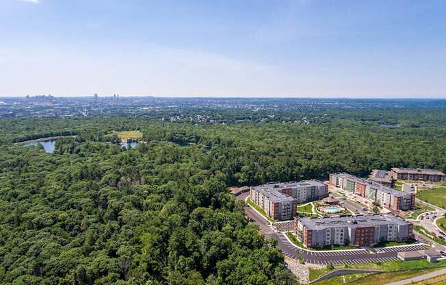 an aerial view of an apartment complex with trees and a city in the distance