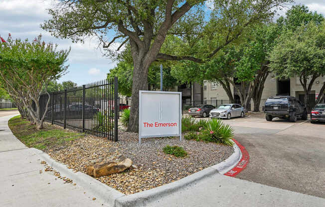 A sign that says The Emerson is in front of a black fence.