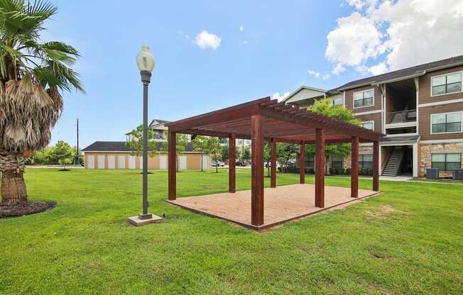 A wooden pavilion is situated in a grassy area in front of a building.