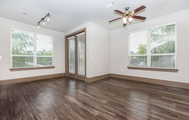 an empty living room with a ceiling fan and two windows